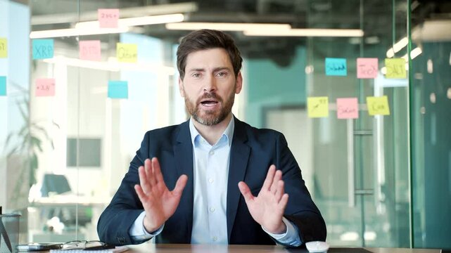 Webcam view. Handsome businessman talking on a video call looking at camera sitting in office. A man in a formal suit has a business meeting, speaks remotely, communicates at an online conference