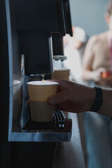 Male hand taking paper cup with coffee from coffee machine at hotel reception