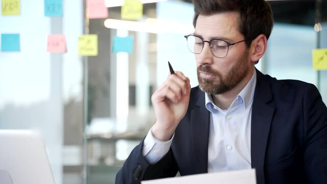 Overworked handsome bearded businessman is bored sitting at workplace at desk in business office. Sleepy exhausted man is tired from working with laptop. A lazy worker procrastinates, gets distracted