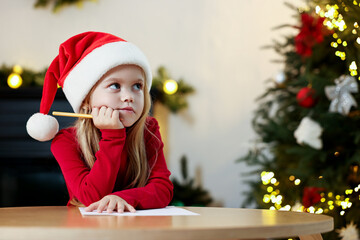 Little girl writing letter to Santa Claus at table indoors. Christmas celebration
