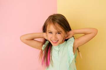 A girl with colored hair laughs merrily looking at the camera on a yellow and pink studio background