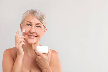 Senior woman with face cream on light background. Space for text