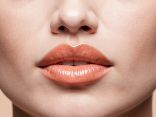 Naklejka premium close up of natural full lips with glossy peach lipstick for beauty concepts.