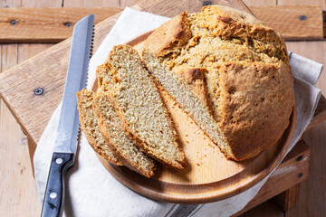 Homemade Irish soda bread cut into pieces and knife on wooden background.
