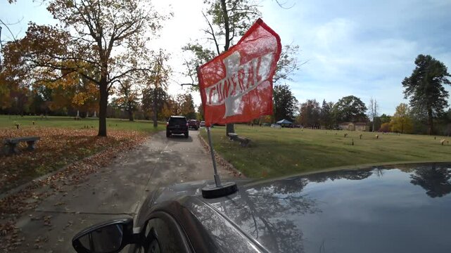 Orange funeral flag on car in procession approaching grave site.