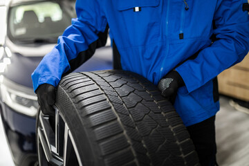 A person in a blue jacket inspects a winter tire at an auto service center during daylight hours