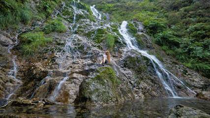 Obraz premium Cascading waterfall flows down a moss-covered rocky hillside.
