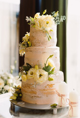 Elegant wedding cake with floral decorations beside a bouquet and wooden box in a sunlit room