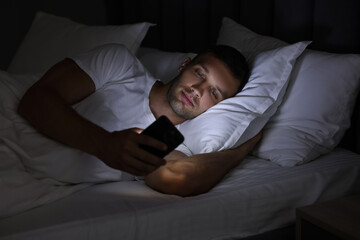 Fototapeta premium Bad habit. Man using smartphone in bed at night