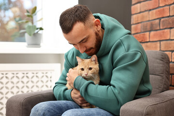 Man petting cute ginger cat on armchair at home