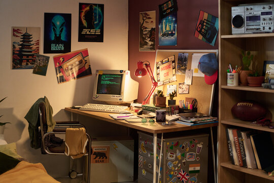 Retro computer setup on desk decorated with vintage posters, various writing tools, and personal items creating nostalgic ambiance