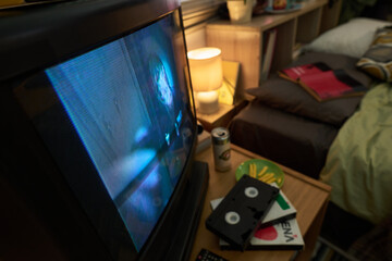 Showing old television playing horror film in cozy bedroom with scattered VHS tapes and a soft...