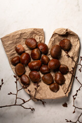 Fresh harvest of edible chestnuts scattered on a on kraft paper with tree branches