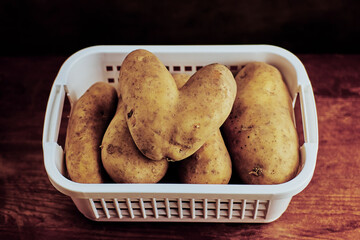still life of a large potato tuber in the shape of a heart lying on other potatoes in a mesh basket on a wooden table, dark background, environmentally friendly concept, close-up