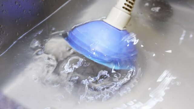 Plunger and A clogged metal kitchen sink. Water does not drain into the water supply due to blockage.