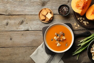 Delicious pumpkin soup in bowl and ingredients on wooden table, flat lay. Space for text