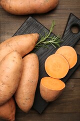 Fresh raw sweet potatoes and rosemary on wooden table, top view