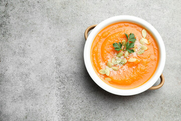 Delicious sweet potato soup with pumpkin seeds and parsley in bowl on grey textured table, top view. Space for text