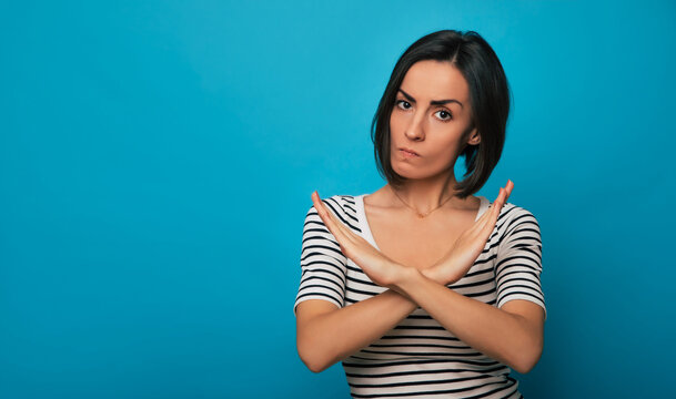 A young woman in a striped shirt crosses her arms in an "X" gesture with a serious expression against a blue background. Her body language communicates disapproval or a firm "no."