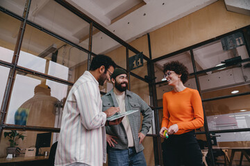 Happy multiethnic colleagues standing by glass wall and discussing in modern office