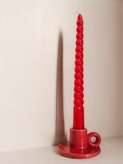 Red candle in a red ceramic candle holder on a light neutral background with copy space