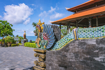 Traditional Balinese griffin statue overlooking the ocean with another statue and temple building...