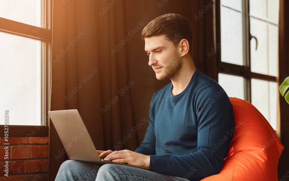 Poster computer work. freelancer man using laptop sitting in beanbag chair in workspace indoor.