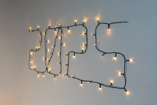 ide view of the "2025" Christmas lights display, with warm yellow bulbs forming the numbers on a white wall. The angled perspective enhances the depth and glow of the lights.
