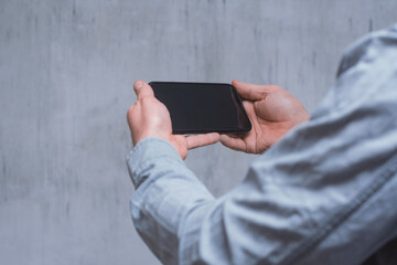 Man holds a mock-up of a smartphone with a dark screen close-up on a concrete background.