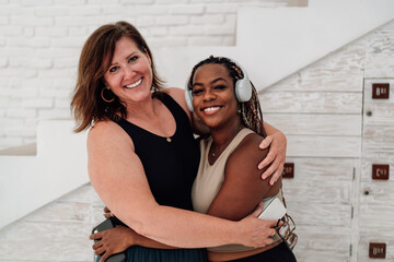 Two women embrace, smiling warmly, radiating positivity and inclusivity. One woman has braided...