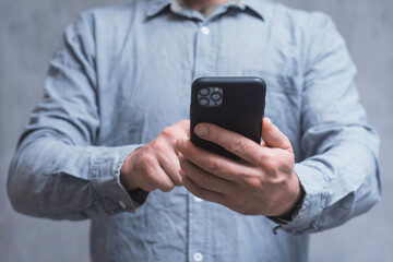 Man holds a mock-up of a smartphone with a dark screen close-up on a concrete background.