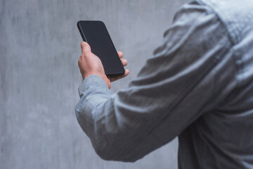 Man holds a mock-up of a smartphone with a dark screen close-up on a concrete background.