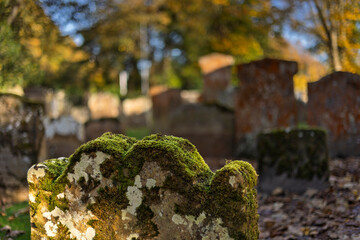 Moss and lichen covered gravestones in old peaceful cemetery with blurry background