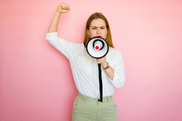 Serious woman raising her fist and shouting through a megaphone on a pink background