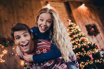 Photo of pretty young couple piggybacl embrace have fun dressed christmas garment tradition atmosphere decor house indoors room