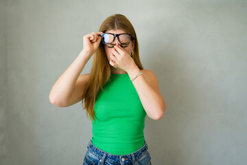 Young woman experiencing eye strain and removing her glasses, experiencing headaches or blurred vision