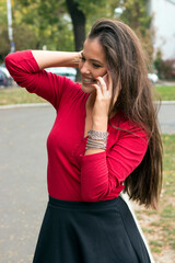Naklejka premium Portrait of a young attractive long haired brunette in red with smartphone in the park