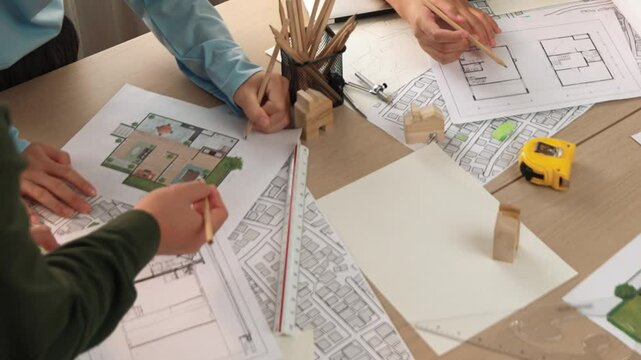 Smart architect and safety engineer discussion about building blueprint on table with architectural document, measurement tools and wooden block scatter around at modern office. Closeup. Delineation.