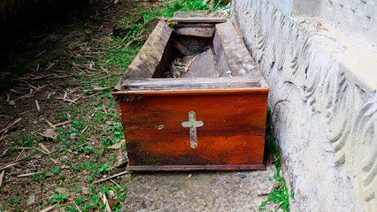 A weathered wooden box with a cross painted on the front, resting against a concrete wall