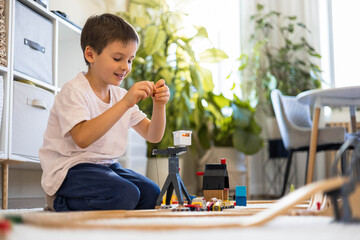 A small white-skinned European child builds a toy railway at home on the carpet. 