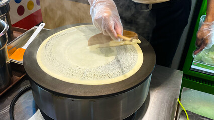 A Person Using a Wooden Spatula to Spread Batter on a Crepe Maker