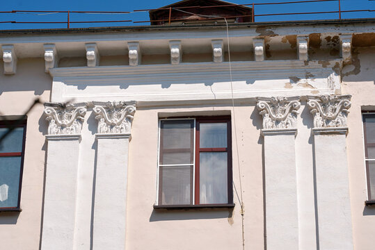 Weathered facade of historic building with decorative columns. pilasters and distressed plaster, highlighting the elegance and deterioration of vintage architecture. View on rough building dentils
