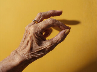 Elderly Woman's Hand with Yellow Nails Giving an 'OK' Gesture on a Bright Yellow Background