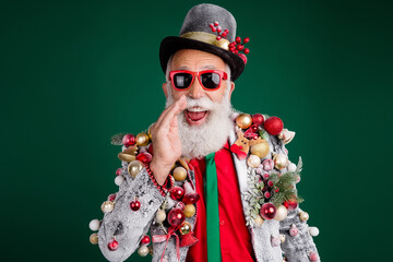 Photo of cool pensioner santa claus share secret cover mouth wear balls baubles on jacket hat sunglass isolated on green color background