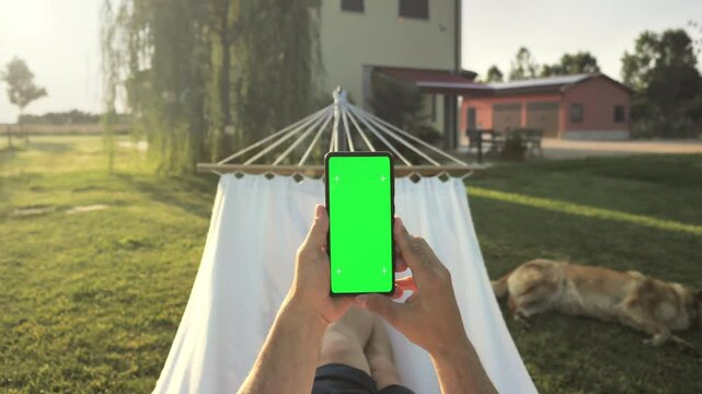 person pov holding smart phone green screen mobile on the hammock,man point of view of smartphone chroma key display in the backyard garden
