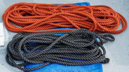 A red rope beside a black rope on a blue tarpaulin on a boat deck.