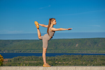 Fitness portrait young athletic woman doing gymnastics on blue sky background