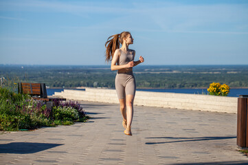 A young woman in a tracksuit performs physical exercises in a summer park
