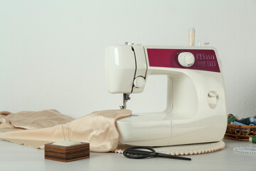 Sewing machine, beige fabric and craft accessories on wooden table indoors