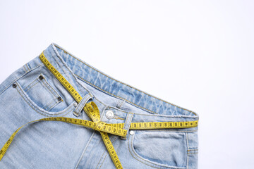 Jeans and measuring tape on white background, top view